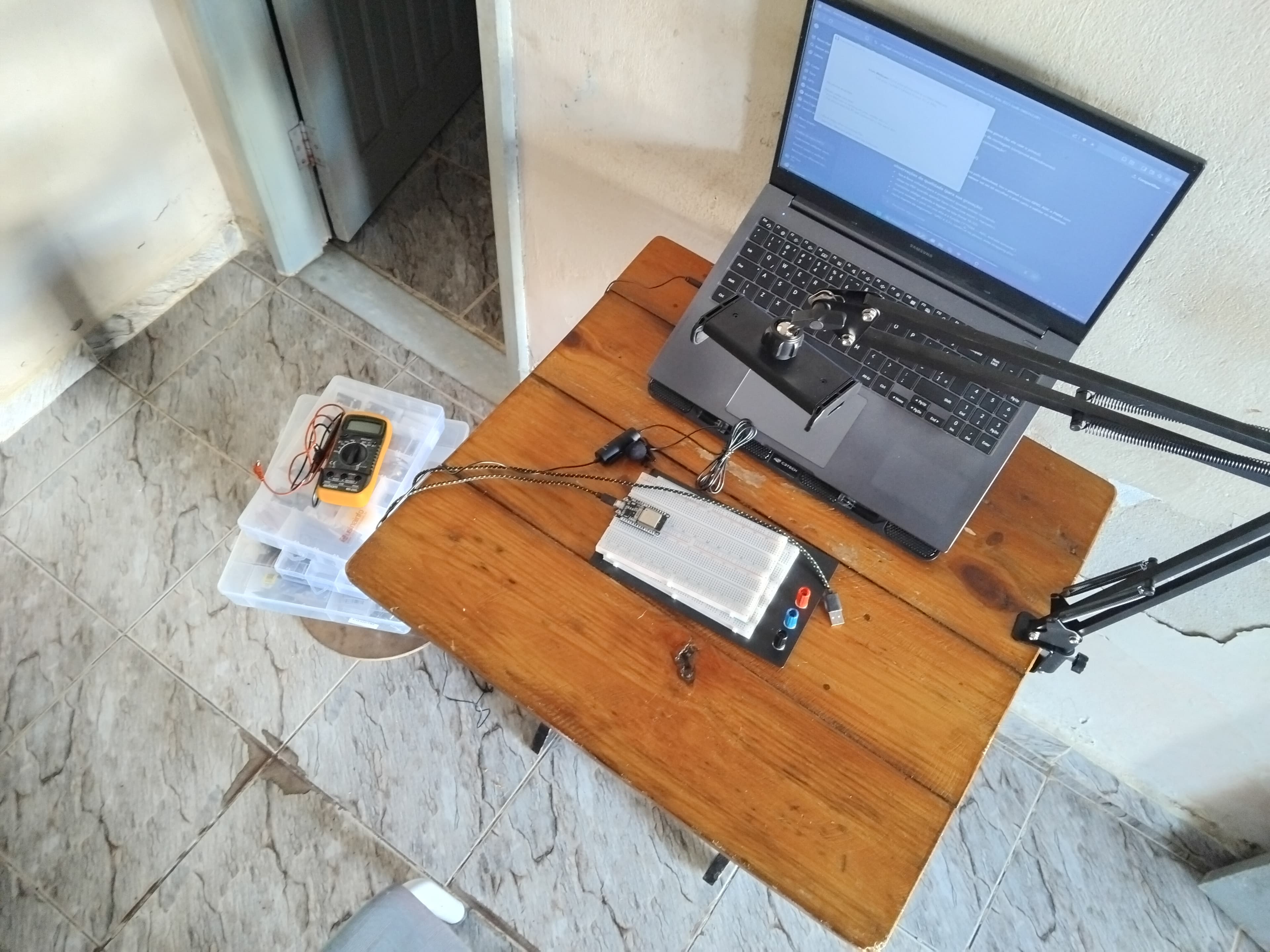 Bancada de desenvolvimento em casa: notebook com editor de código aberto, protoboard com ESP32, multímetro e caixa de componentes